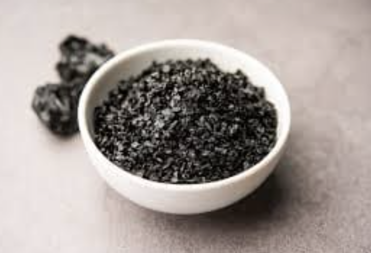 Granular shilajit resin in a bowl beside raw pieces